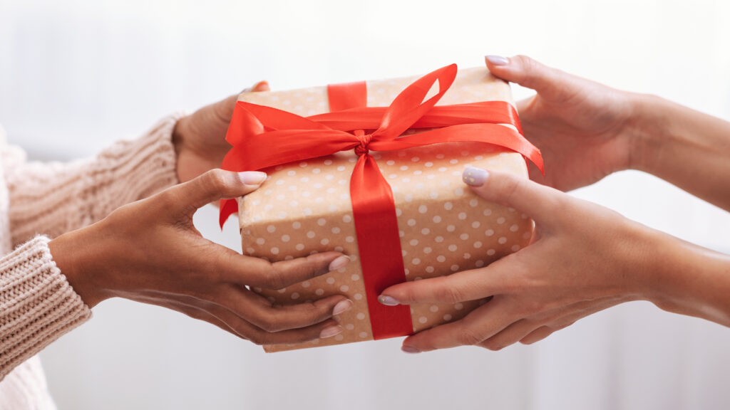 Family And Friendship Concept. Closeup of unrecognizable black woman giving gift box with red ribbon to her female friend, lady receiving present, celebrating holiday indoors at home