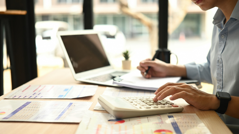 Close-up view of a Business analyst, a man using a calculator to evaluate financial charts and documents on a desk.