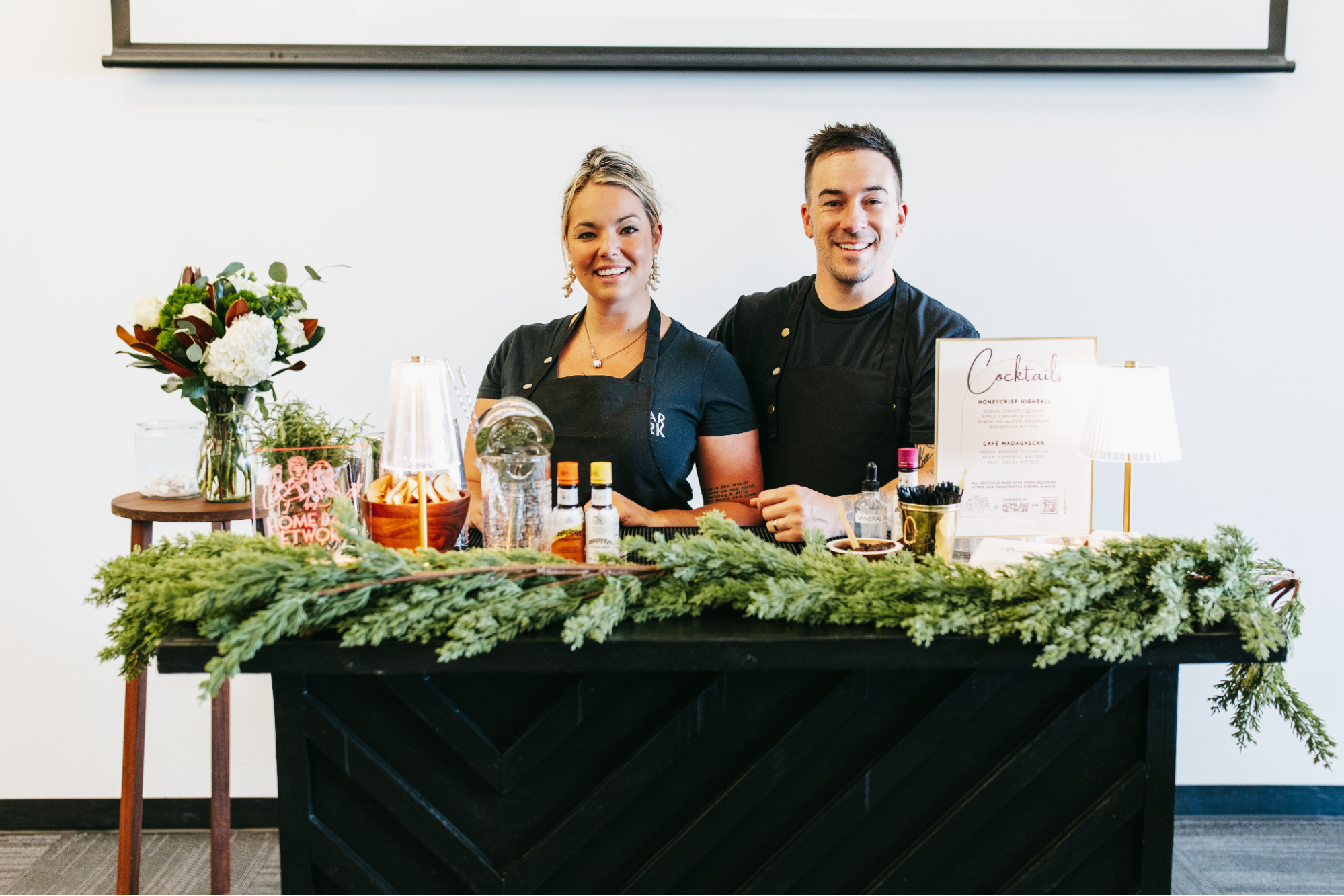 Two bartenders behind a bar decorated for holidays.