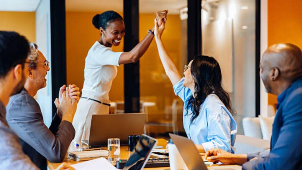 Employees gathered around a table with two people giving each other a high five.